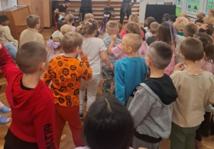 Dzieci stoją na sali gimnastycznej podczas koncertu zespołu, Pani ręce uniesione w górze.